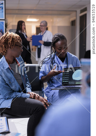 Nurse and patient analyzing brain scan on laptop, talking about tomography diagnosis and neural system on computer. Young woman and medical assistant doing checkup consultation in waiting room lobby. Nurse and patient analyzing brain scan on laptop, talking about tomography diagnosis and neural system on computer. Young woman and medical assistant doing checkup consultation in waiting room lobby. 94653519