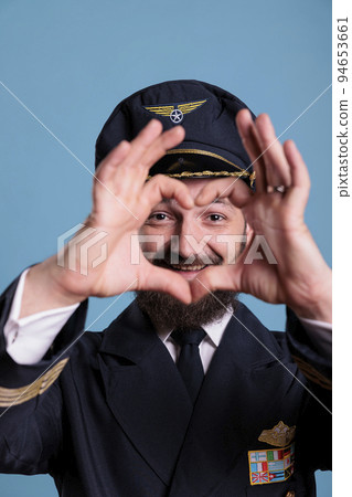 Smiling airliner pilot showing heart shaped love symbol with fingers, conceptual romance gesture. Friendly airplane aviator in uniform expressing affection feelings front view medium shot Smiling airliner pilot showing heart shaped love symbol with fingers, conceptual romance gesture. Friendly airplane aviator in uniform expressing affection feelings front view medium shot 94653661