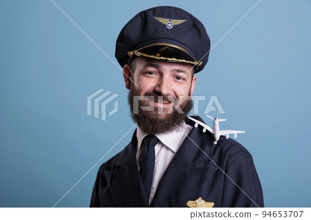 Smiling pilot in uniform with airplane model on shoulder portrait, aviation academy aviator playing with small plane. Aircraft crew member with commercial jet toy, looking at camera 94653707