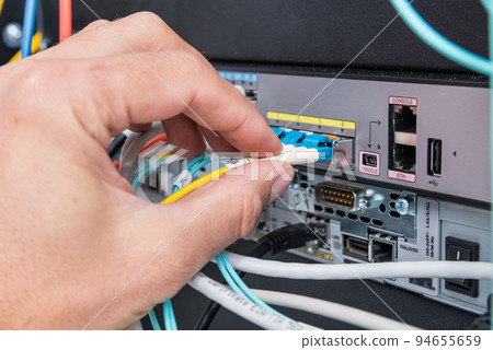 Hand of computer technician connecting fiber optics cable into data switch 94655659