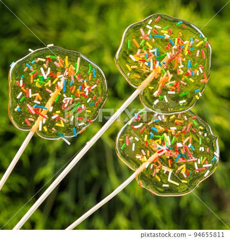 three transparent lollipops, with multi-colored sugar crumbs, against a background of natural greenery three transparent lollipops, with multi-colored sugar crumbs, against a background of natural greenery 94655811