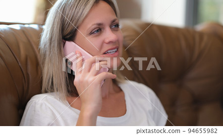 Pretty woman is sitting on couch talking on mobile phone Pretty woman is sitting on couch talking on mobile phone 94655982