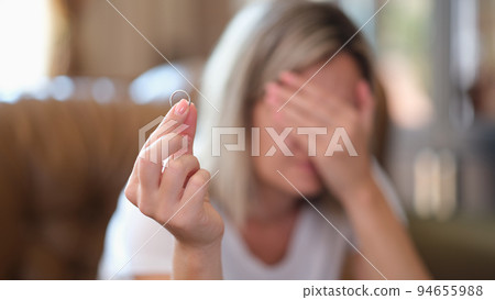 Upset woman holding engagement ring and thinking about dissolution of marriage or divorce 94655988