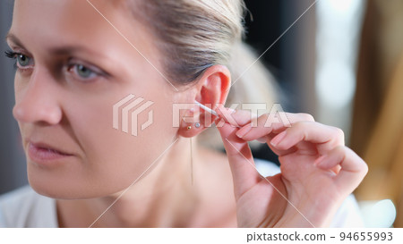 Closeup of young woman cleaning ear with cotton swab Closeup of young woman cleaning ear with cotton swab 94655993