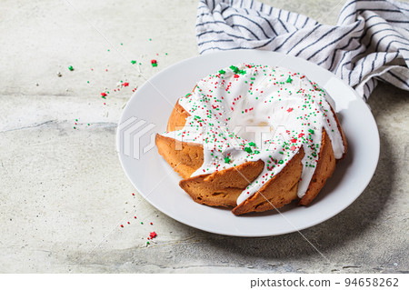 Christmas dessert. Vanilla pound cake with sugar icing and festive colored sprinkles on white plate, gray background. 94658262