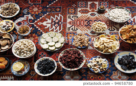 Eastern feast. Asian still life of dried fruits and nuts in plates on a carpet 94658780