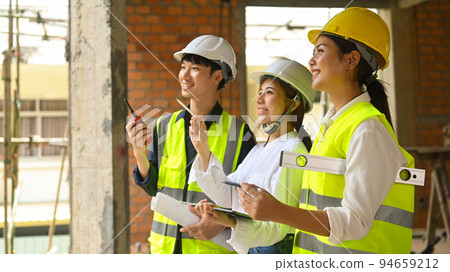 Smiling female investor and engineer managers wearing safety helmet working, checking plan together at construction site 94659212