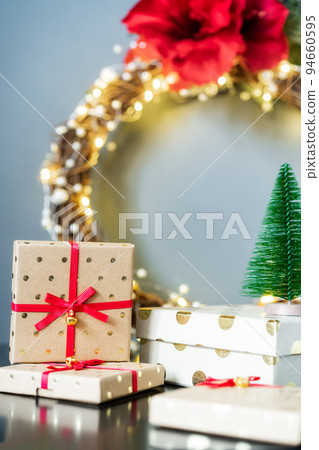 Christmas composition with gift boxes, red lantern, small Christmas trees decor and elegant flower wreath on black table on gray wall background. Festive home decor. Scandinavian style. Copy space 94660595