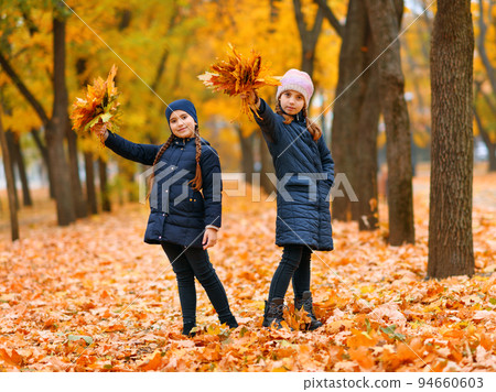 Girls playing and posing in autumn city park. Two children plays with yellow maple leaves. Fall season, beautiful nature with yellow trees. Girls playing and posing in autumn city park. Two children plays with yellow maple leaves. Fall season, beautiful nature with yellow trees. 94660603