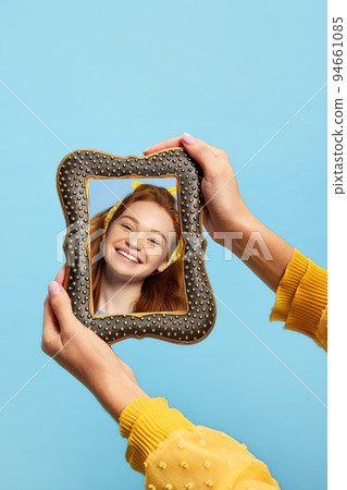 Young redheaded girl holding vintage style mirror in her hands and looking at her reflection. Concept of beauty, emotions, art Young redheaded girl holding vintage style mirror in her hands and looking at her reflection. Concept of beauty, emotions, art 94661085
