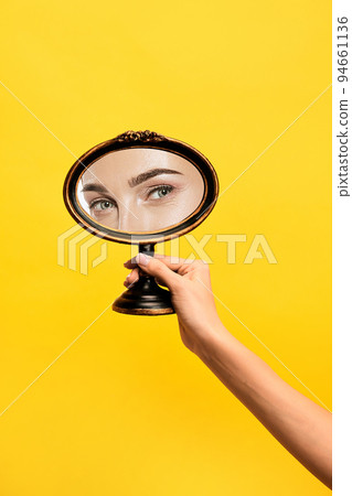 Happy look. Female hand holding mirror with reflection of girl's eyes isolated over yellow background. Concept of style, beauty, art Happy look. Female hand holding mirror with reflection of girl's eyes isolated over yellow background. Concept of style, beauty, art 94661136
