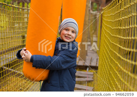 boy plays on the playground, overcomes an obstacle, holds an orange bag and smiles, sport concept 94662059