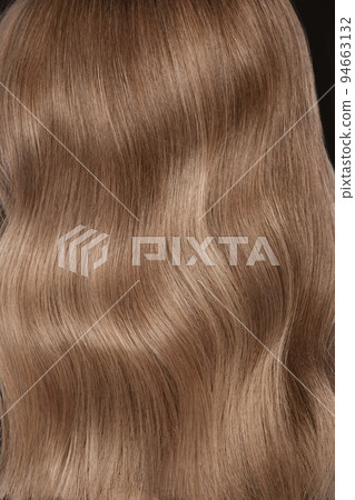 A closeup view of a bunch of shiny straight blond hair in a wavy curved style A closeup view of a bunch of shiny straight blond hair in a wavy curved style 94663132