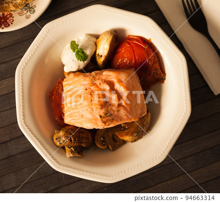 simmered slice of salmon with tomato spinon and coconut sauce in a white bowl. top view simmered slice of salmon with tomato spinon and coconut sauce in a white bowl. top view 94663314