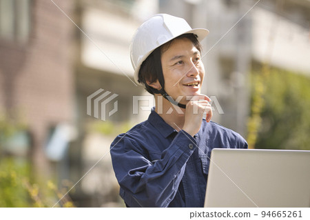 一個穿著工作服的男人在建築工地看電腦 一個穿著工作服的男人在建築工地看電腦 94665261