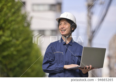 一個穿著工作服的男人在建築工地看電腦 94665265
