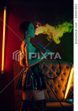 Sexy brunette model is smoking a hookah exhaling a smoke at a luxury night club. 94665802