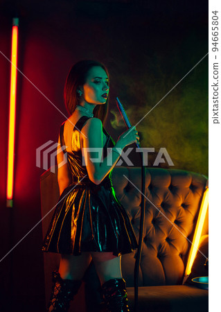 Sexy brunette model is smoking a hookah exhaling a smoke at a luxury night club. Sexy brunette model is smoking a hookah exhaling a smoke at a luxury night club. 94665804