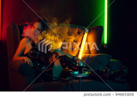 Sexy brunette model is smoking a hookah exhaling a smoke at a luxury night club. Sexy brunette model is smoking a hookah exhaling a smoke at a luxury night club. 94665808