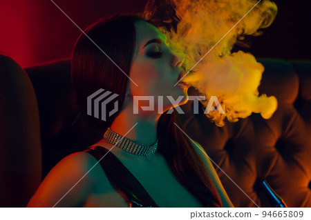 Sexy brunette model is smoking a hookah exhaling a smoke at a luxury night club. 94665809