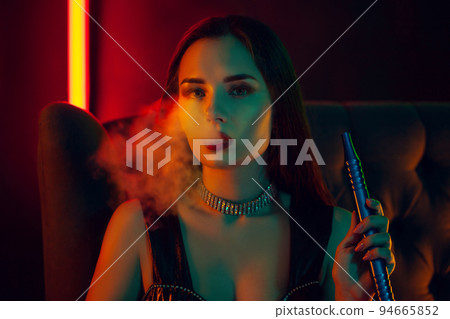 Sexy brunette model is smoking a hookah exhaling a smoke at a luxury night club. Sexy brunette model is smoking a hookah exhaling a smoke at a luxury night club. 94665852