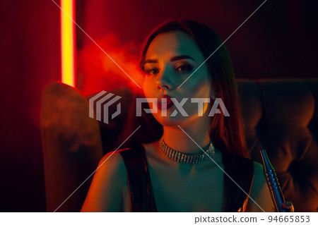 Sexy brunette model is smoking a hookah exhaling a smoke at a luxury night club. Sexy brunette model is smoking a hookah exhaling a smoke at a luxury night club. 94665853