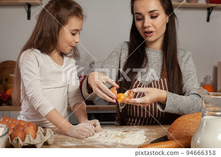 Mother and her daughter are baking a bread and having fun at the kitchen. 94666358