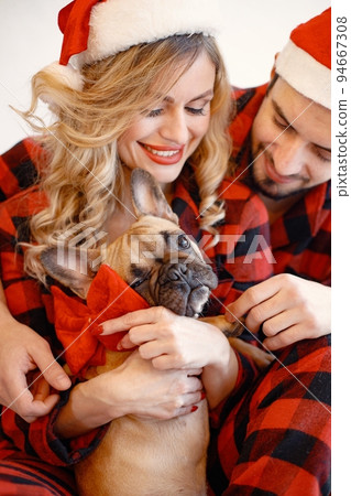 Portrait of lovely couple celebrating christmas with dog. Blonde woman and brunette man wearing plaid pajamas. French bulldog with his family. 94667308