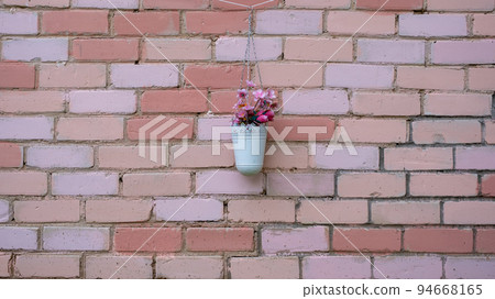 In natural light, a flower pot is hung on a painted brick wall. In natural light, a flower pot is hung on a painted brick wall. 94668165