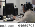 African American designer in headphones draws on tablet 3D models for games. 94669708