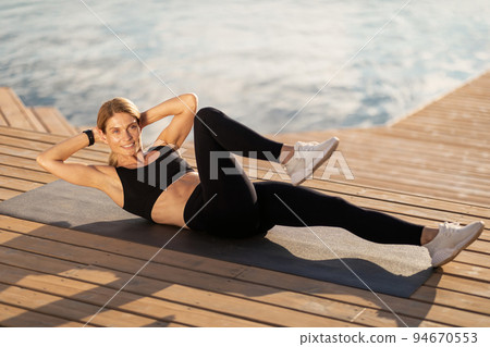 Athletic Middle Aged Woman Doing Elbow-To Knee Crunches Exercise While Training Outdoors 94670553
