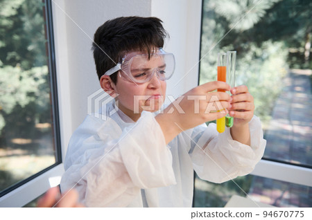Curious smart school child, elementary age boy wearing safety goggles and lab gown,holds test tubes with colorful reagents and chemicals, watching the chemical reaction going on. Learning Chemistry Curious smart school child, elementary age boy wearing safety goggles and lab gown,holds test tubes with colorful reagents and chemicals, watching the chemical reaction going on. Learning Chemistry 94670775