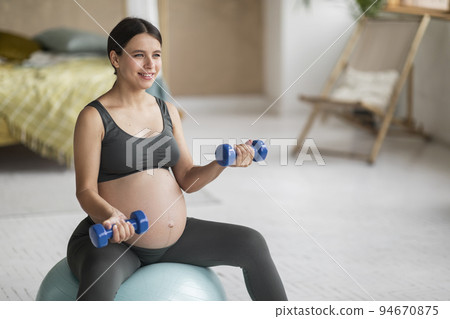 Beautiful Young Pregnant Woman Sitting On Fitball And Training With Dumbbells 94670875