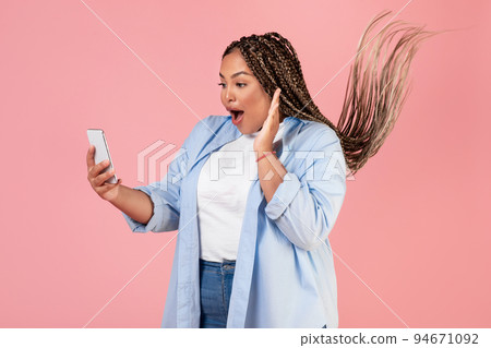 Excited African American Female Holding Cellphone Standing Over Pink Background Excited African American Female Holding Cellphone Standing Over Pink Background 94671092