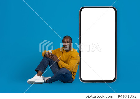 Cheerful african american man sitting on floor, using cell phone Cheerful african american man sitting on floor, using cell phone 94671352