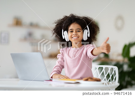Black girl schooler using laptop and headphones, showing thumb up 94671416