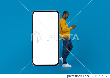 Happy african american man leaning on big smartphone, mockup 94671467