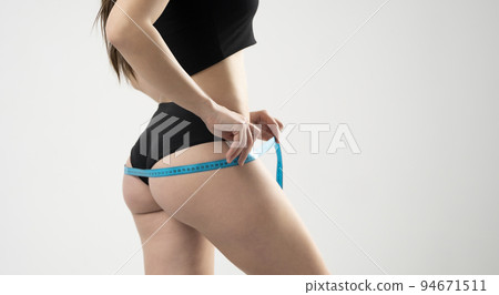 Young woman in black underwear is measuring her thigh with measuring tape on white background. 94671511