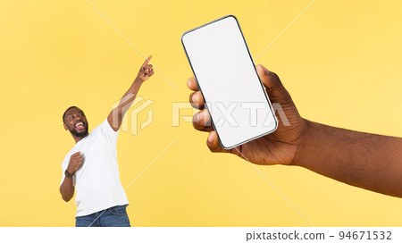 Black Man Pointing At Huge Cellphone In Hand, Yellow Background Black Man Pointing At Huge Cellphone In Hand, Yellow Background 94671532