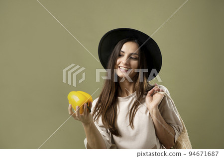 Smile brunette woman in a black hat carrying the shopping net eco bag on the soulder containing of organic vegetable and holds yellow pepper in hand. Enjoy healthy life shopping. Smile brunette woman in a black hat carrying the shopping net eco bag on the soulder containing of organic vegetable and holds yellow pepper in hand. Enjoy healthy life shopping. 94671687