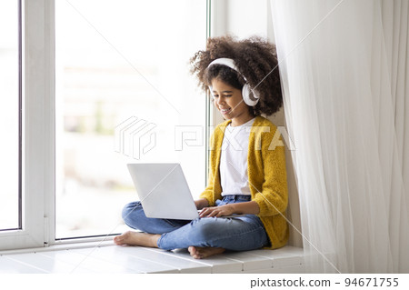 Cute little black girl with wireless headphones using laptop 94671755
