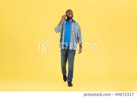 African Guy Talking On Phone Communicating Walking Over Yellow Background 94672317