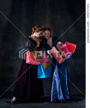 Portrait of two beautiful women in image of queens isolated over dark background. Big shopping season Portrait of two beautiful women in image of queens isolated over dark background. Big shopping season 94672501