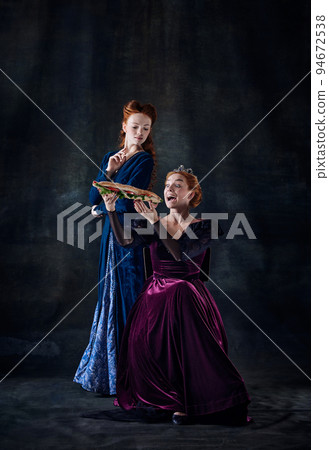 Portrait of two beautiful women in image of royal persons isolated over dark background. Queen eating big sandwich Portrait of two beautiful women in image of royal persons isolated over dark background. Queen eating big sandwich 94672538