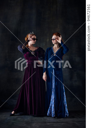 Portrait of two beautiful women in image of queens posing in stylish sunglasses isolated over dark background Portrait of two beautiful women in image of queens posing in stylish sunglasses isolated over dark background 94672561