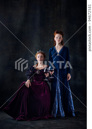 Portrait of two beautiful women in image of queens isolated over dark background. Royal family legacy Portrait of two beautiful women in image of queens isolated over dark background. Royal family legacy 94672581