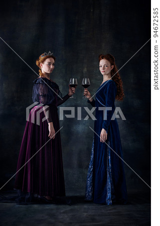 Portrait of two beautiful women in image of queens with wine glasses isolated over dark background Portrait of two beautiful women in image of queens with wine glasses isolated over dark background 94672585