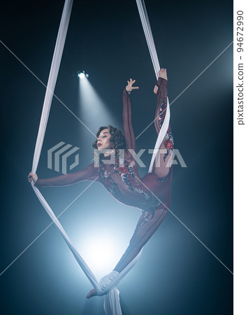 A young girl performs the acrobatic elements in the aerial silk. Studio shooting performances on a black background A young girl performs the acrobatic elements in the aerial silk. Studio shooting performances on a black background 94672990