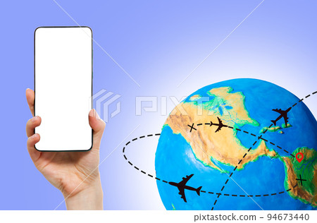 Global transportation. Planet Earth with a silhouettes of an airplanes flying along the routes. Hand holding a smartphone with mock up, copy space. The concept of air travel Global transportation. Planet Earth with a silhouettes of an airplanes flying along the routes. Hand holding a smartphone with mock up, copy space. The concept of air travel 94673440