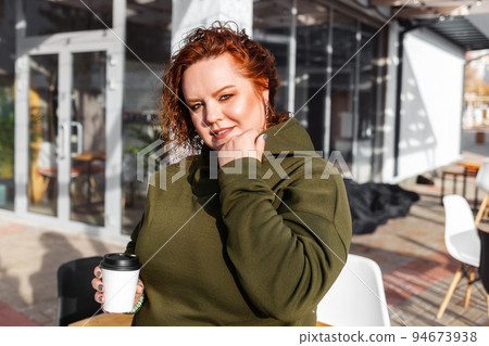 Portrait of a overweight smiling woman posing with a cup of coffee in her hand. Cafe at the background. Concept of psychology 94673938